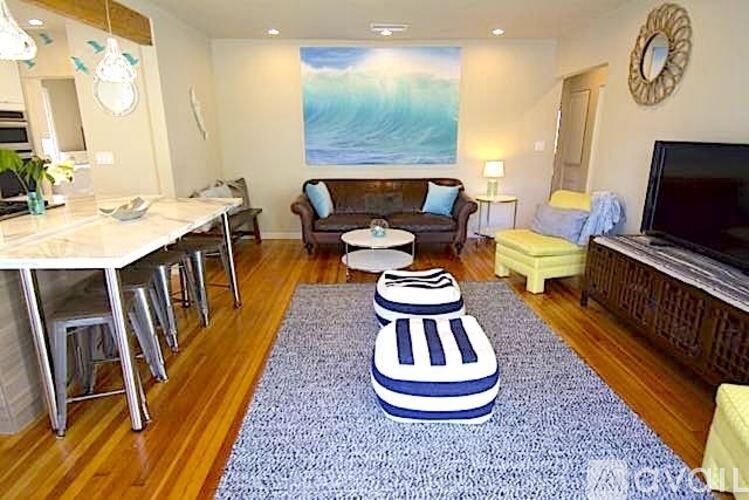 A living room with a blue rug and a painting of a wave on the wall.