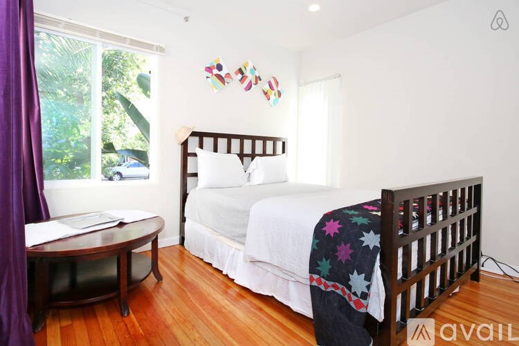 A bedroom with a bed, a round table, and a window with purple curtains.