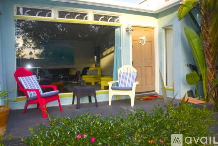 A red chair sits on a porch with a blue wall and a wooden door.
