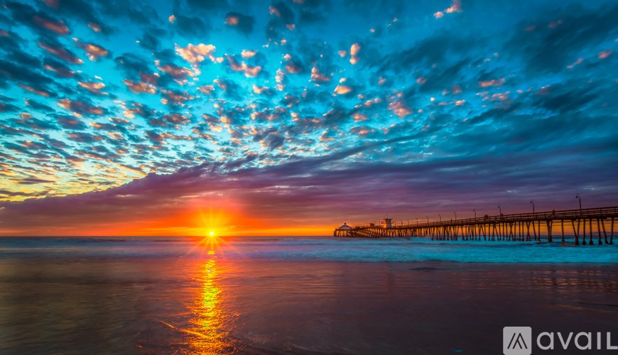 A beautiful sunset over the ocean with a pier in the distance.