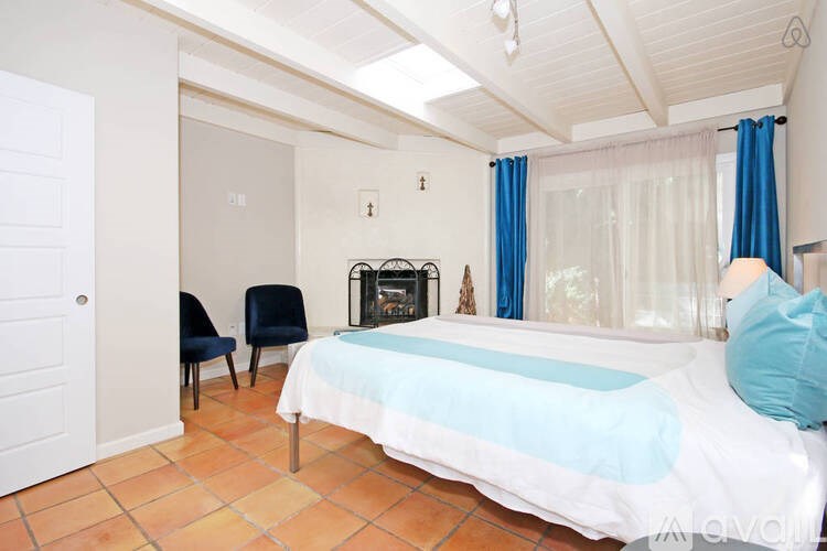 A bedroom with a bed, chair, and fireplace.