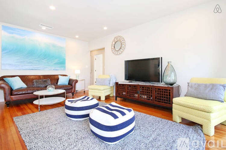A living room with a leather couch, a wooden cabinet, and a large painting of a wave on the wall.