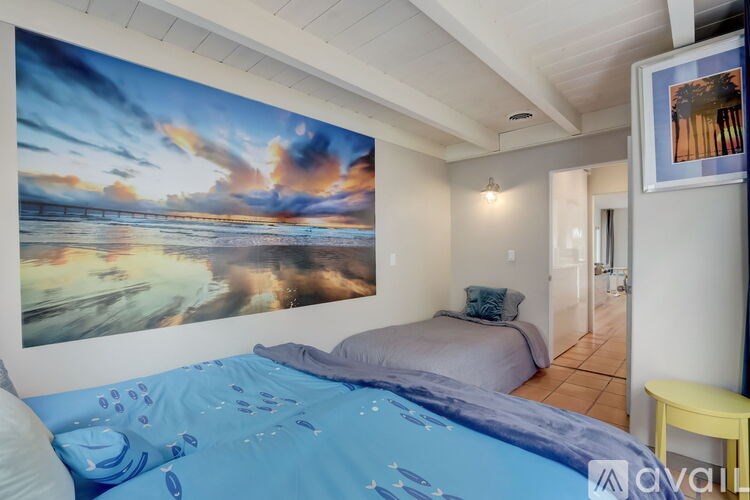 A bedroom with a large bed and a painting of a sunset on the wall.
