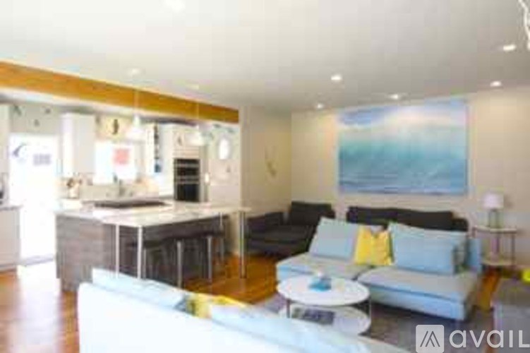 A modern living room with a white sofa and a kitchen area in the background.