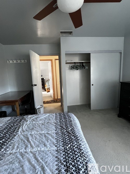 A bedroom with a bed in the foreground and a closet with clothes hanging in the background.