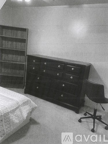 A black and white photo of a bedroom with a bed, dresser, and chair.