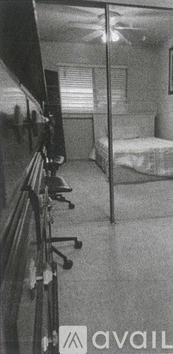 A black and white photo of a room with a bed, a desk, and a chair.