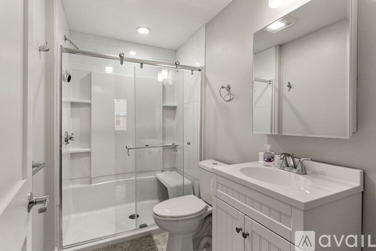 A white bathroom with a toilet, sink, and glass shower stall.