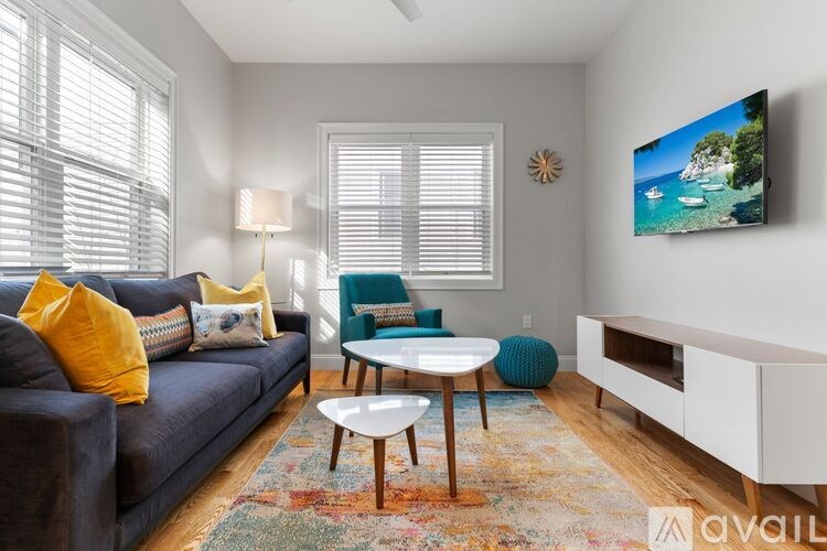 A living room with a grey couch, a blue chair, a white coffee table, and a painting on the wall.