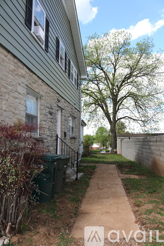 A house with a green trash can and a tree in the yard.