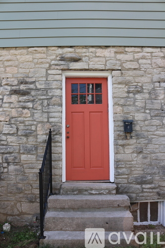 A red door with a black railing and a stone wall.