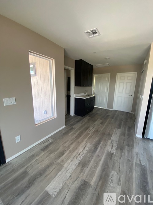 A room with wooden flooring and a kitchen area in the background.