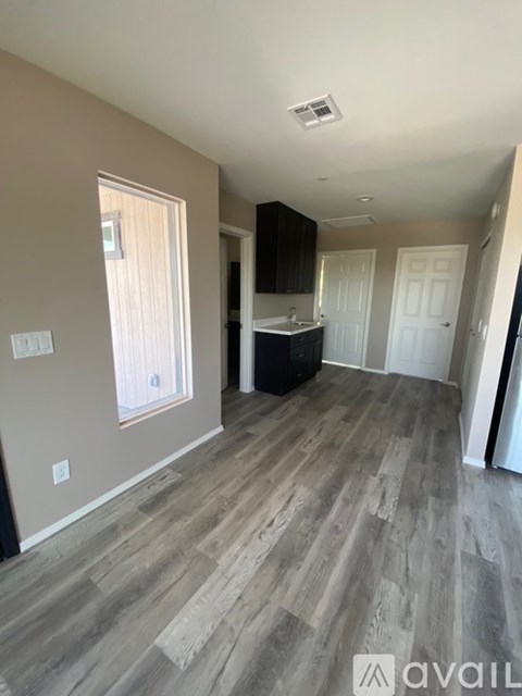 A room with wooden flooring and a kitchen area in the background.