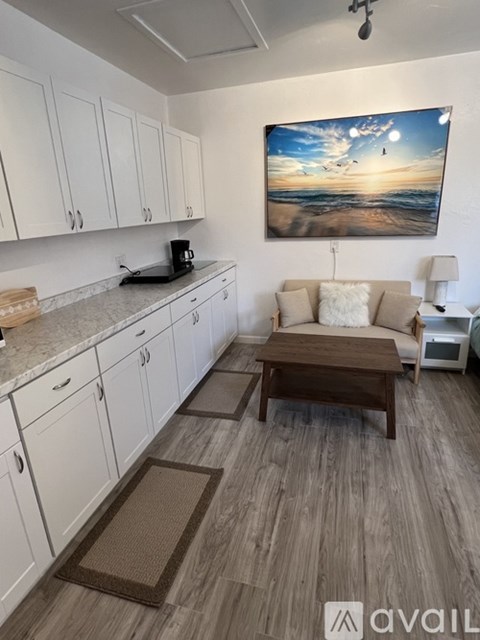 A kitchen with white cabinets and a painting of a beach scene on the wall.