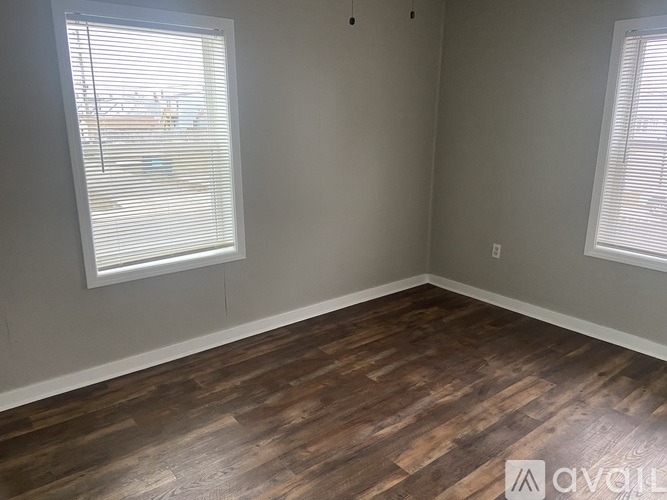 A room with wooden flooring and two windows.