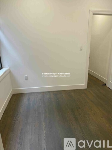 A room with wooden flooring and a white wall with a window.