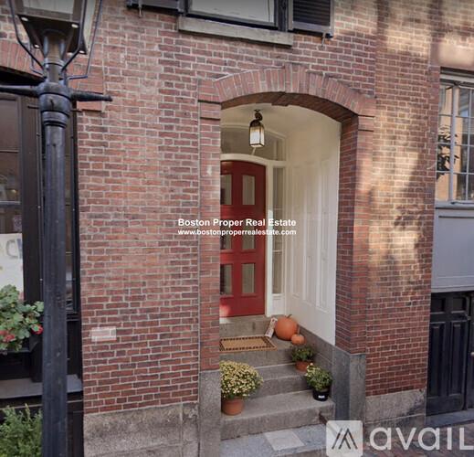 A red door is on the left side of a brick building.
