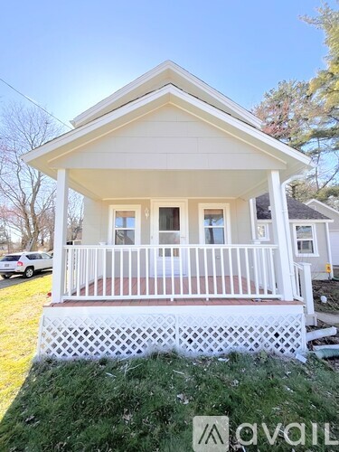 A white house with a porch and a car parked in the background.