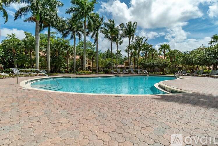 A pool surrounded by palm trees and a brick patio.