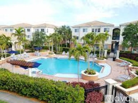 A swimming pool surrounded by a green hedge and palm trees.