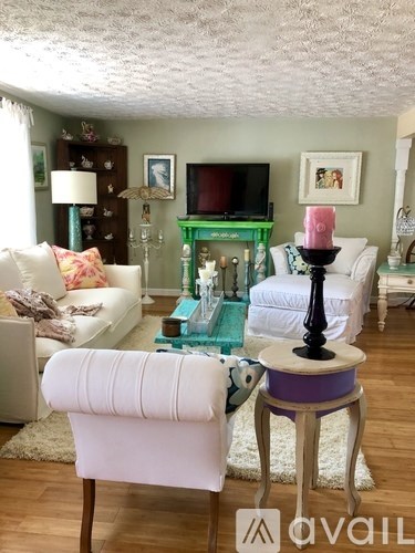 A living room with a white couch, a green fireplace, and a purple stool.