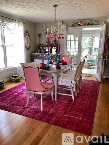 A dining room with a table set for four and chairs with a red rug on the floor.