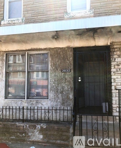 A black door with a metal grill is on the right side of a building with a window and a balcony.