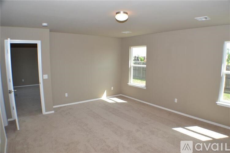 A room with a carpeted floor, a ceiling light, and a window with a view of trees and a fence.