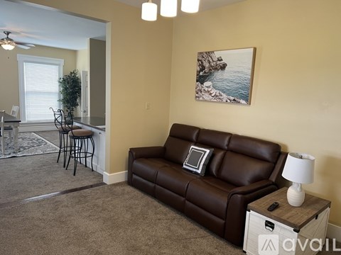 A living room with a brown leather couch, a small table with a lamp, and a painting on the wall.