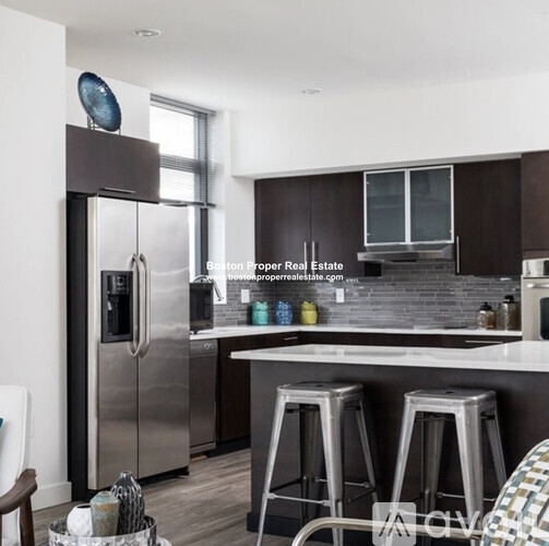 A modern kitchen with a stainless steel refrigerator and bar stools.
