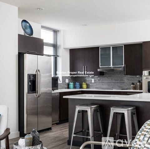 A modern kitchen with a stainless steel refrigerator and bar stools.