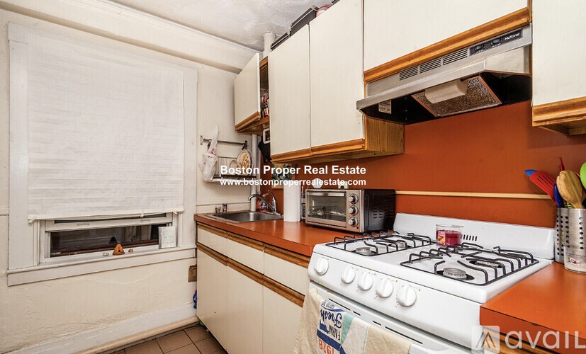A kitchen with a white stove and a window with blinds.