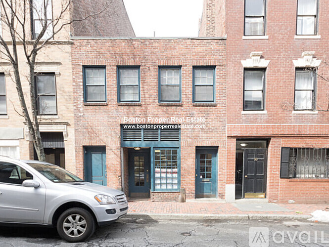 A silver car is parked in front of a red brick building.