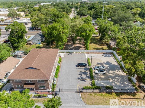 A parking lot is surrounded by a building and trees.