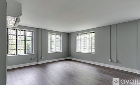 A spacious room with wooden floors and two windows.