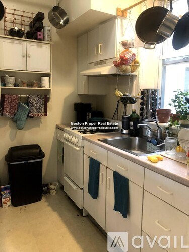A kitchen with white cabinets and a black trash can.
