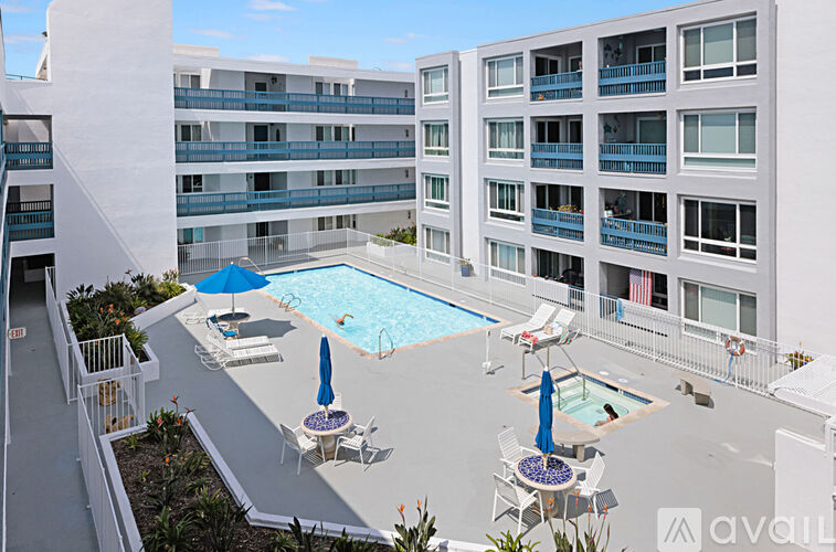 A pool area with chairs and umbrellas in front of apartment buildings.
