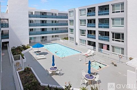 A pool area with chairs and umbrellas in front of apartment buildings.