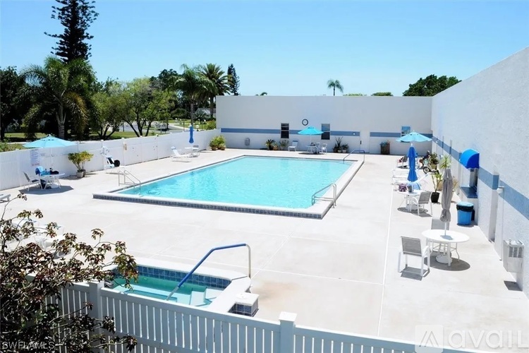 A pool and patio area with a white fence and trees in the background.