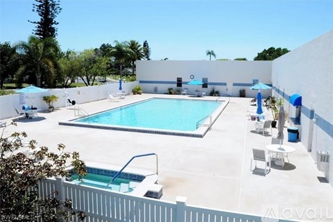 A pool and patio area with a white fence and trees in the background.