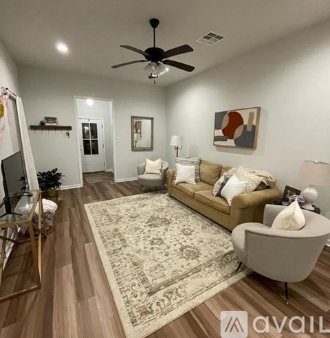 A living room with a beige sofa, a rug, a ceiling fan, and a painting on the wall.