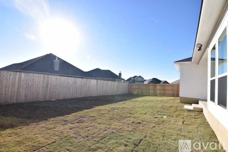 A backyard with a wooden fence and a house on the right side.