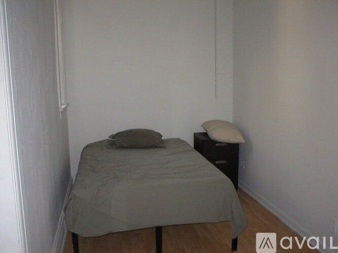 A bed with a grey cover and a small white pillow is in a room with a wooden floor.