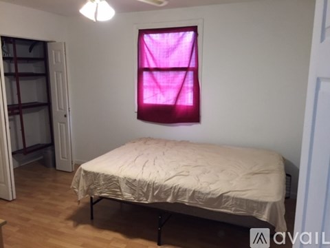 A bedroom with a bed, a window with a pink curtain, and a wooden floor.
