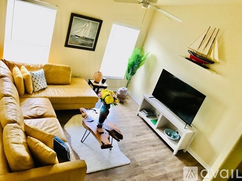A living room with a yellow couch, a television, and a small table with a vase of flowers on it.