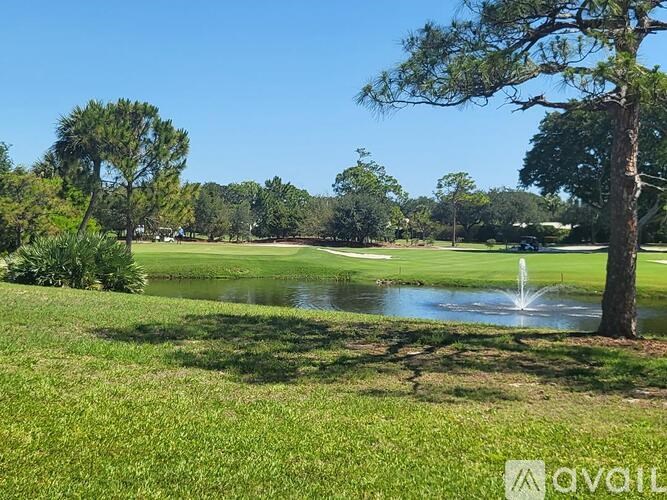 A pond with a fountain in the middle of a grassy area with trees in the background.