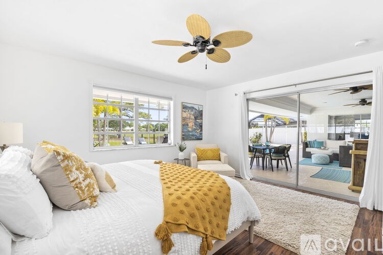 A bedroom with a bed, a ceiling fan, and a view of the backyard through the window.