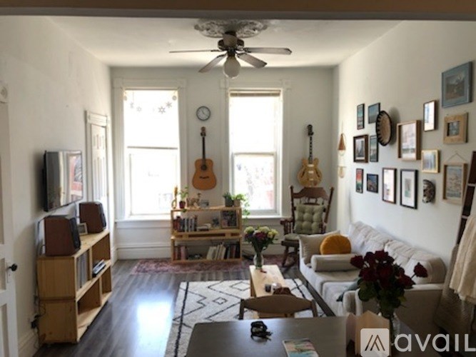 A living room with a couch, a guitar, a fan, and a rug.