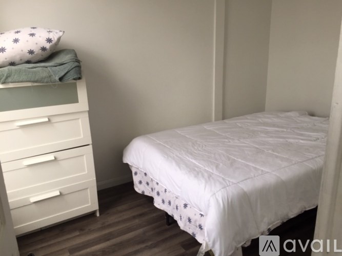A white bed with a white pillow and a white nightstand with drawers.
