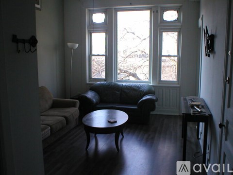 A living room with a black leather couch, a grey couch, a round table, and a window with a view of trees outside.